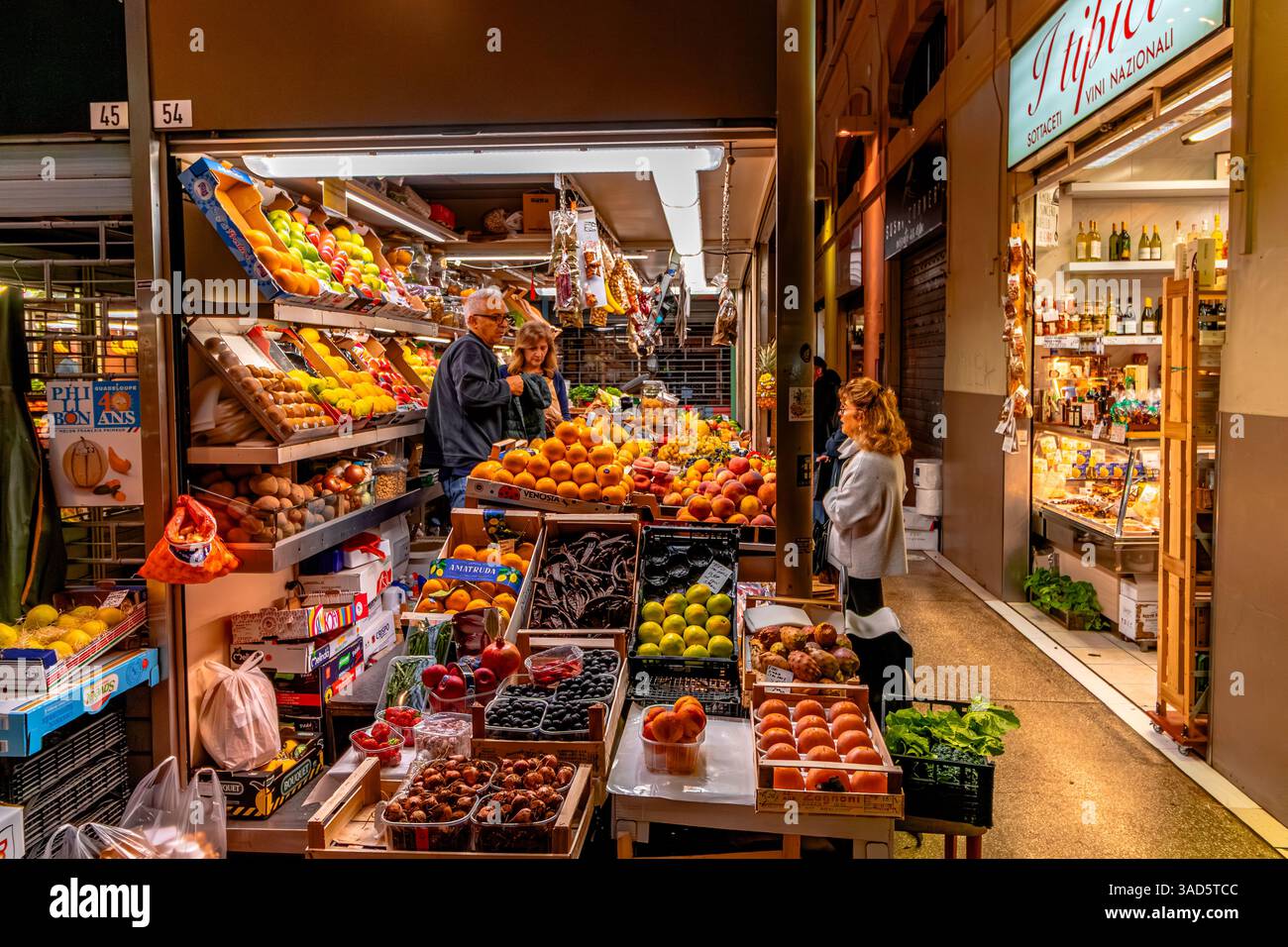 Persone che fanno acquisti di frutta e verdura in una stalla all'interno del mercato delle Erbe, un grande mercato coperto nel centro storico di Bologna, Italia Foto Stock