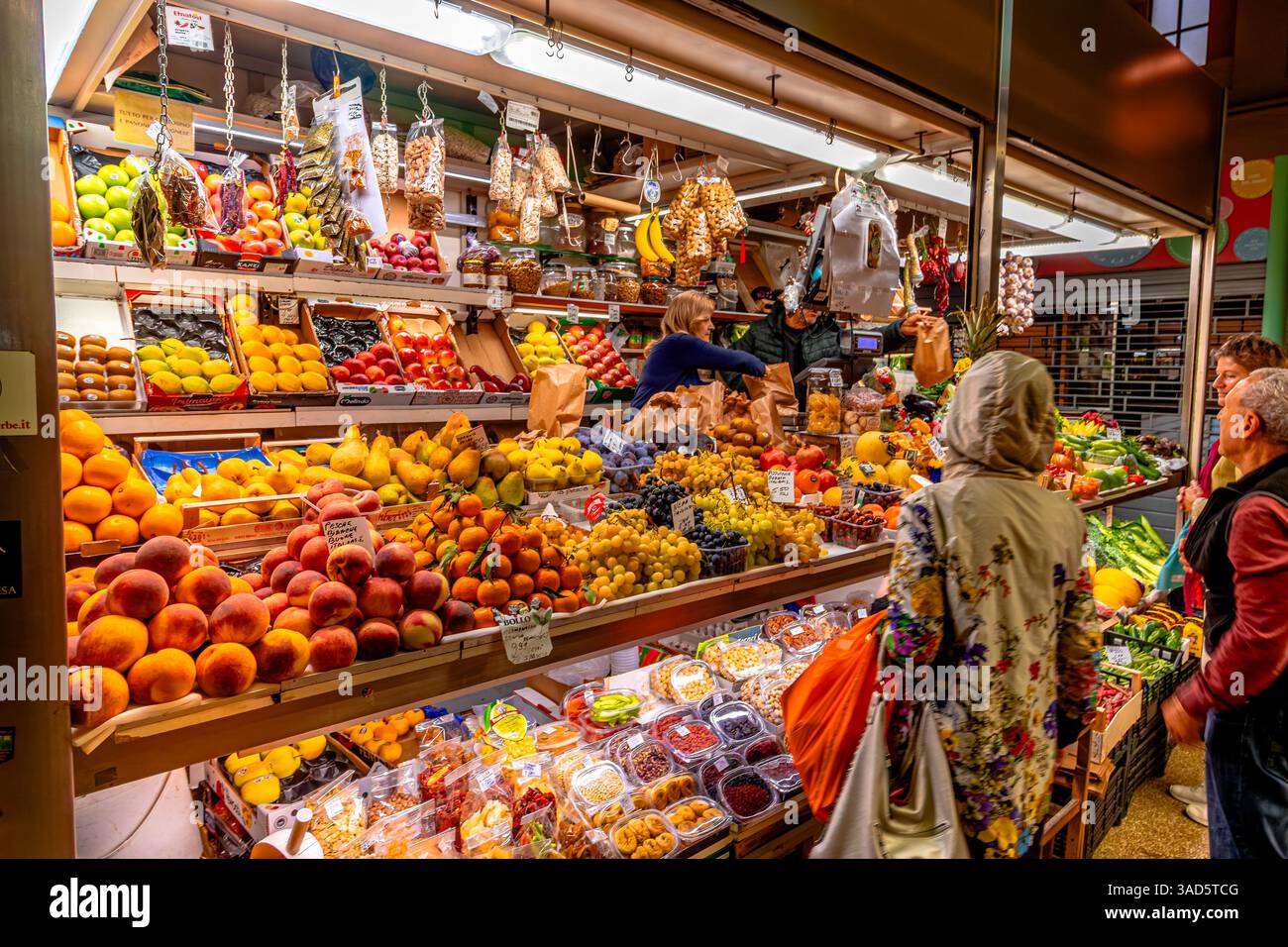 Persone che fanno acquisti di frutta e verdura in una stalla all'interno del mercato delle Erbe, un grande mercato coperto nel centro storico di Bologna, Italia Foto Stock