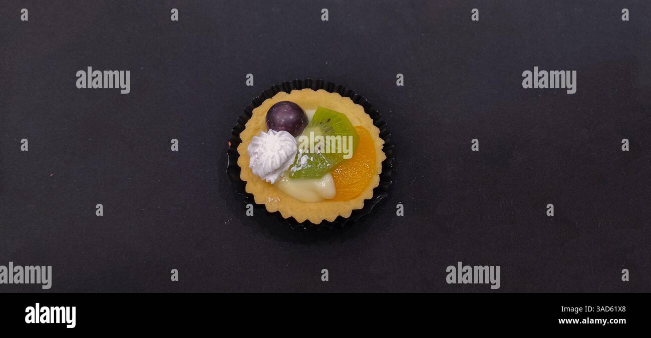 crostata di frutta splendidamente decorata con kiwi, arancia e uva, condita con panna, perfetta per dessert, cottura al forno e fotografia del cibo Foto Stock
