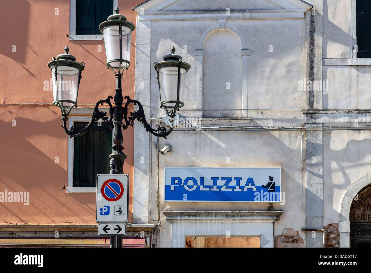 Chioggia, Italia - 3 marzo 2025: Cartello della polizia Nazionale Italiana sulla facciata di un edificio storico, con semafori e segnaletica stradale Foto Stock
