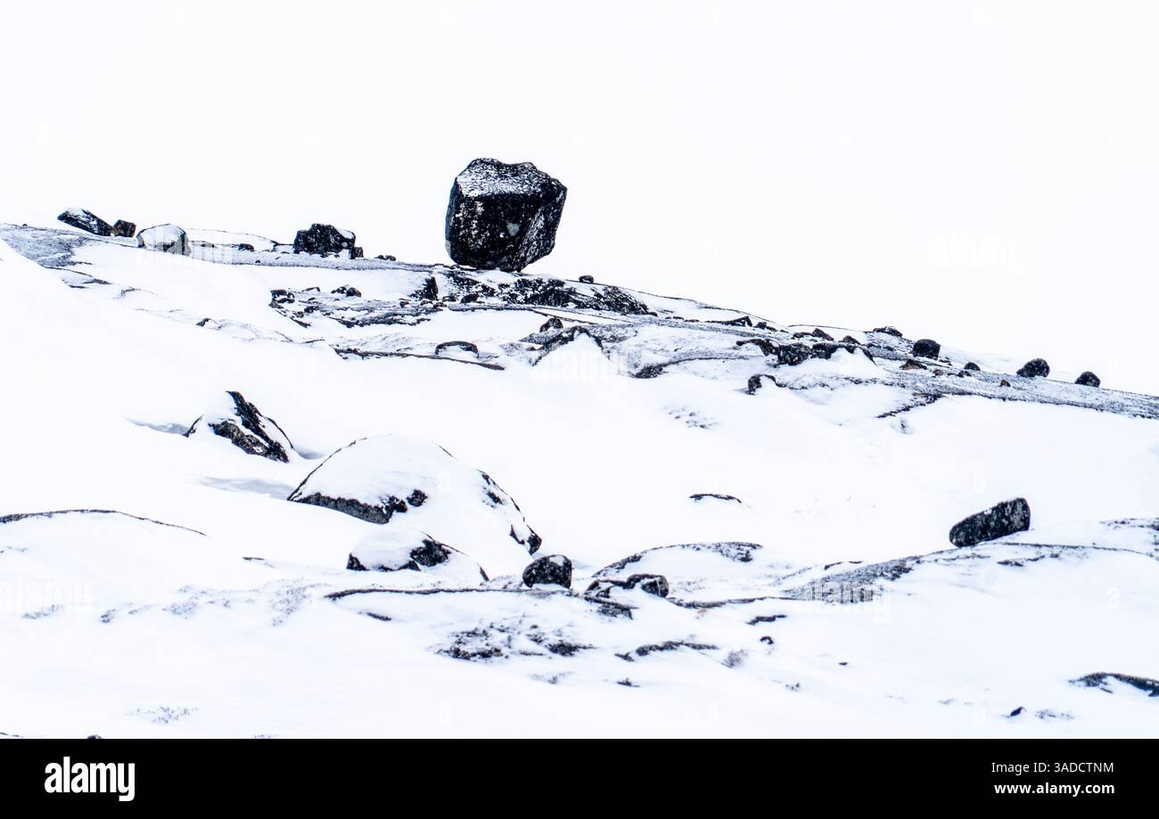 Un masso solitario arroccato su un paesaggio innevato, circondato da rocce più piccole e da una coperta di neve. La scena è minimalista con uno sfondo bianco, Foto Stock