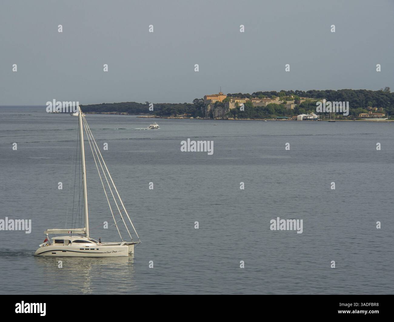 Barca a vela in acque calme con un'isola sullo sfondo sotto un cielo leggermente nuvoloso, cannes, il mar mediterraneo, la francia Foto Stock