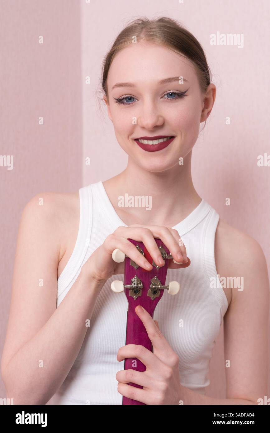 Ritratta giovane musicista felice con ukulele, il suo volto è pieno di gioia e guarda la macchina fotografica con un sorriso sincero. Bella donna positiva Foto Stock