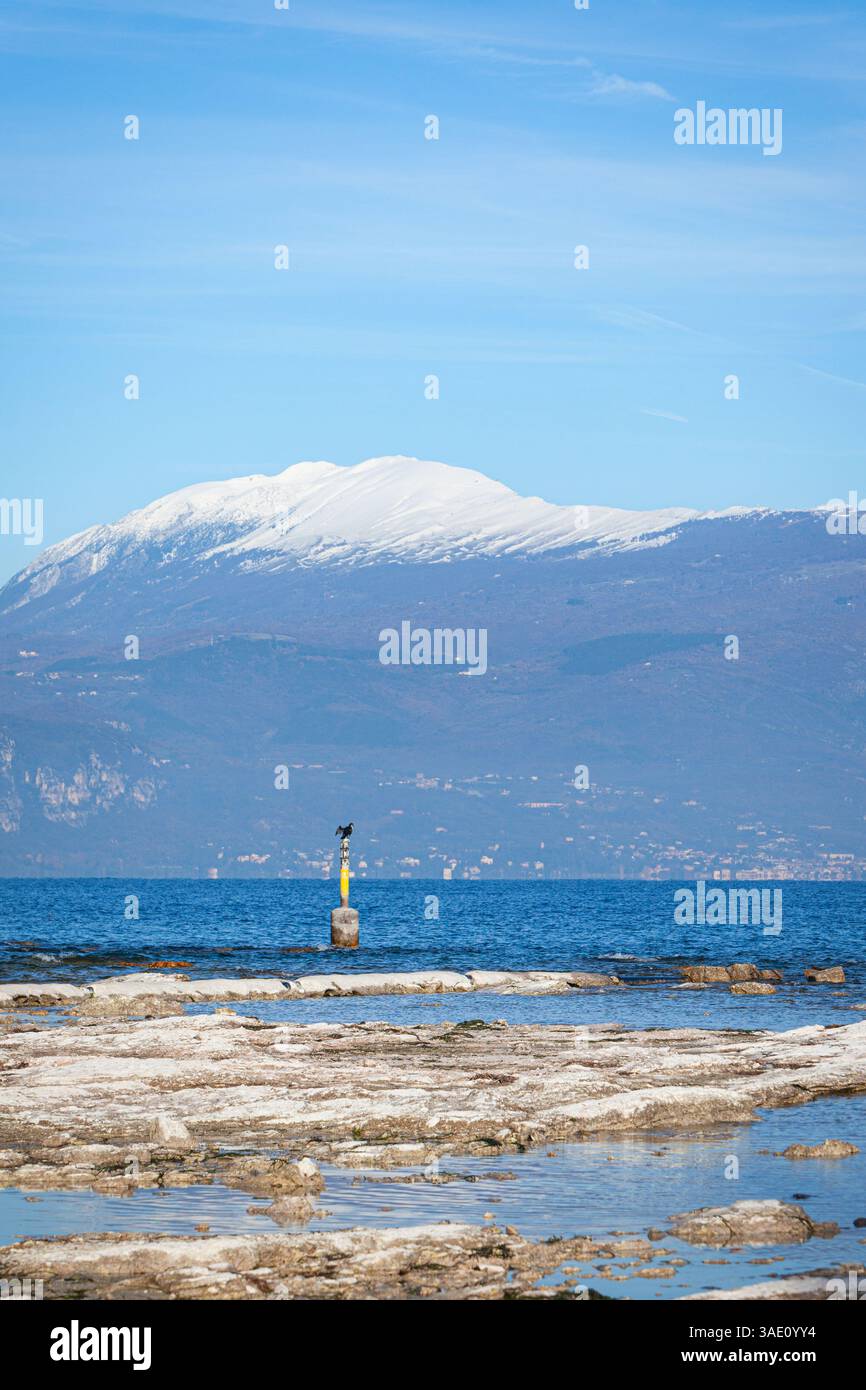 Il litorale del Lago di Garda vicino a Sirmione in Lombardia, Italia settentrionale, con le cime innevate delle Alpi italiane visibili sul retro. Foto Stock