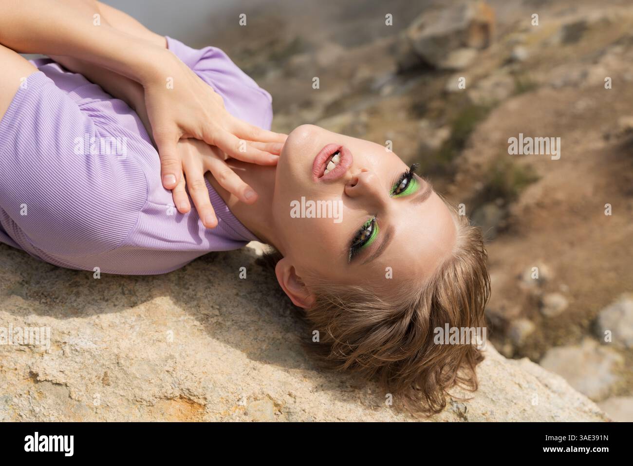 La splendida modella femminile si trova sulla roccia in montagna, mette entrambe le palme sul collo e guarda la fotocamera. Magnifica sensualità caucasica Foto Stock