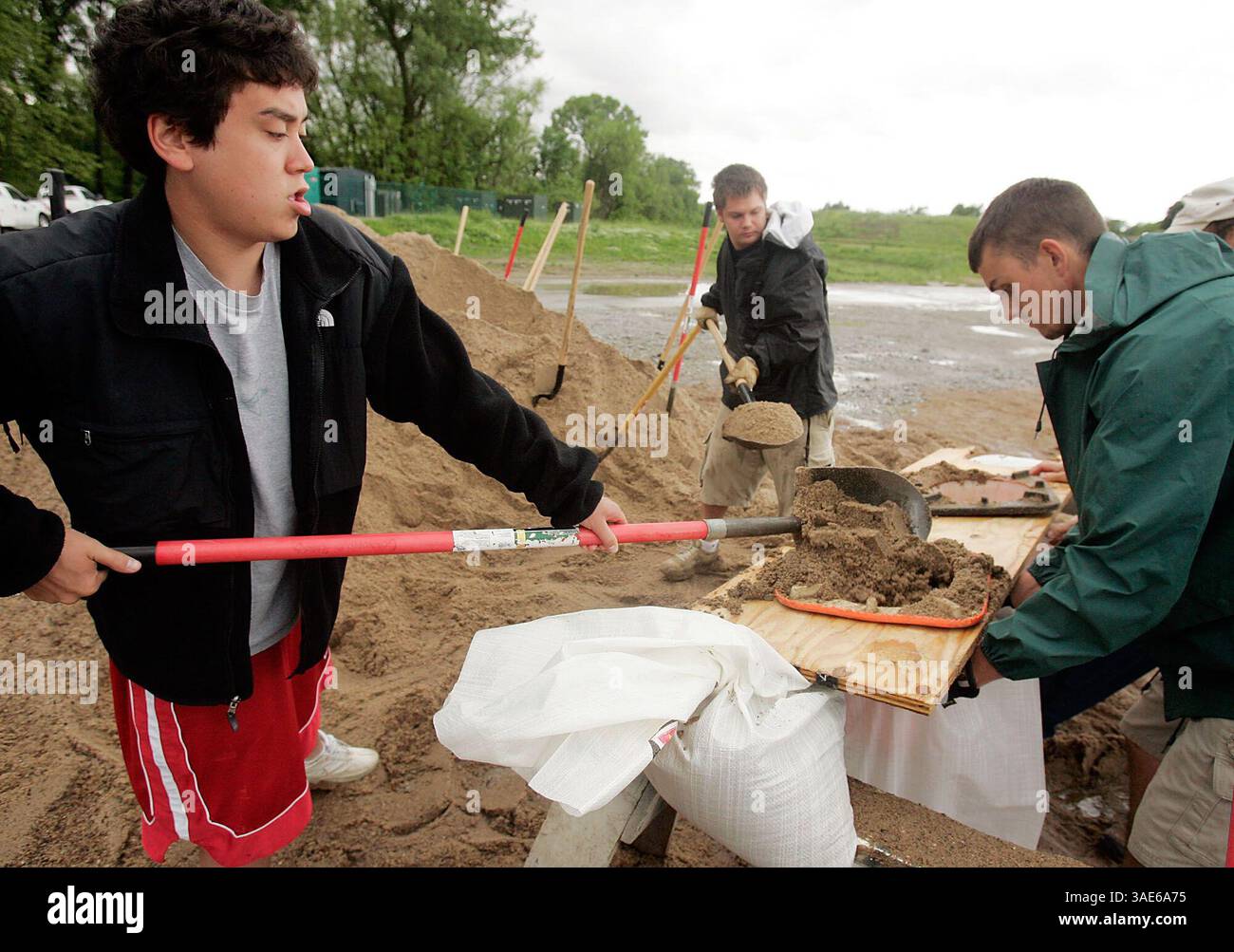 5 giugno 2008 - Coralville, Iowa, USA - dipendenti di Coralville Parks and Rec A.J. Blancaflor e Dustin Getta pala sabbiosa mentre Cameron Boyce tiene uno dei sacchi di sabbia all'angolo di Quarry Rd E E. 7th St. A Coralville. L'inondazione sul fiume Iowa è prevista presso la vicina Edgewater Drive dopo che il flusso d'acqua fuori dalla dannazione del lago Coralville è aumentato questa mattina per evitare che il lago trabocchi il passaggio. Gli operai comunali hanno indicato che Coralville ha rilasciato un comunicato stampa stamattina chiedendo volontari per aiutare con il sandbagging. Migliaia di persone sono fuggite dalle inondazioni nel mi degli Stati Uniti Foto Stock