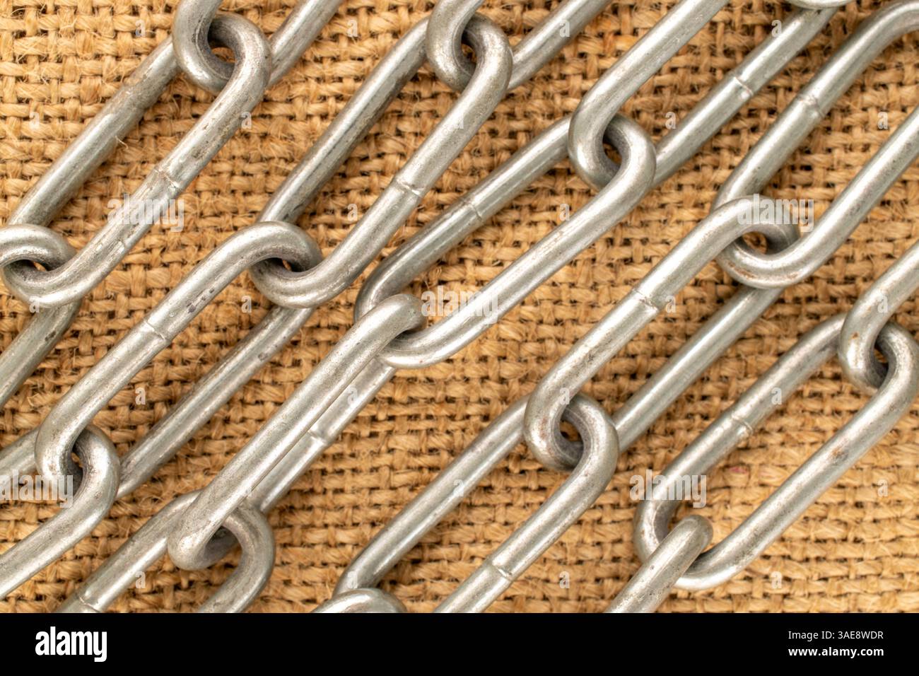 Un pezzo di catena metallica su tessuto di iuta, macro, vista dall'alto. Foto Stock