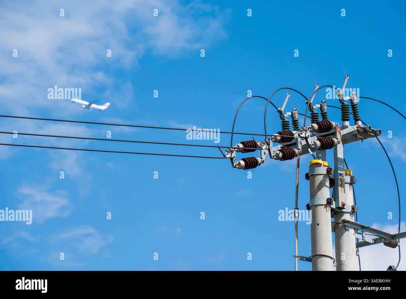 Dettagli tecnologici, dell’infrastruttura della rete energetica con cielo blu e velivolo sullo sfondo. Fili e connettori. Foto Stock