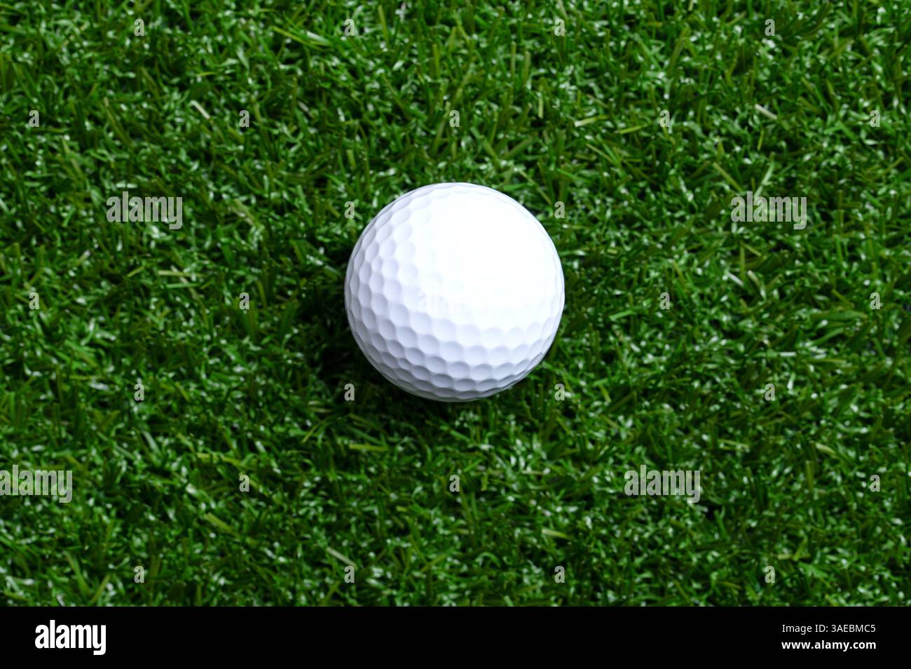 Palla da golf su erba artificiale, primo piano. Palla da golf americana bianca singola con tacche speciali, su una superficie piana in erba di plastica. Foto Stock