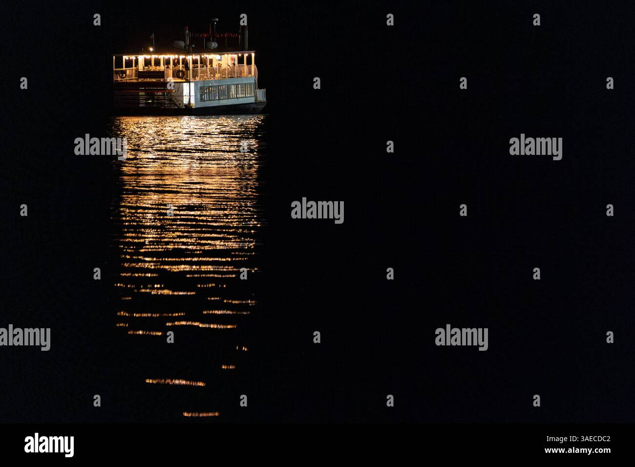 Le luci di un tour in barca con una ruota a pale che si riflettono sull'acqua. Foto Stock