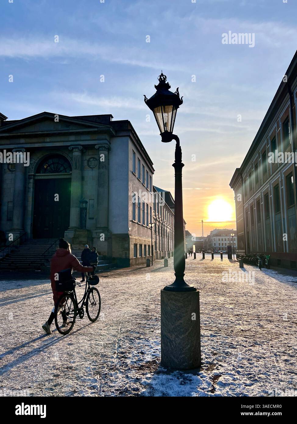 Tramonto a Copenaghen vicino al Palazzo di Christianborg. Una persona che cammina una bicicletta e un antico lampione stradale. In una giornata invernale e innevata con un cielo azzurro. Foto Stock