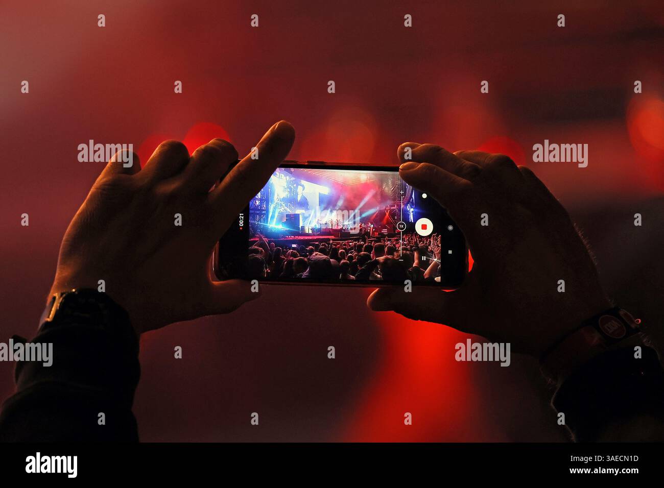 Mano di un uomo in piedi nel pubblico che registra un video ad un concerto con un telefono Foto Stock