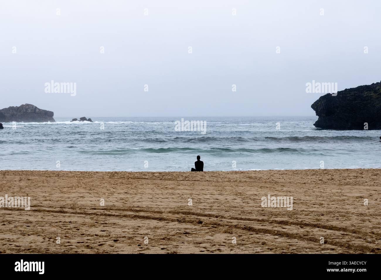 Un surfista solitario in piedi sulla sabbia di una spiaggia nelle Asturie, nel nord della Spagna, a guardare le onde dell'Oceano Atlantico. Foto Stock