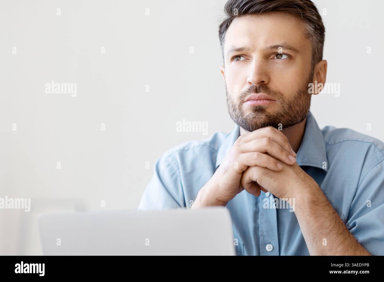 Ritratto di uomo d'affari pensivo seduto al lavoro con il laptop e. Guardando via Foto Stock