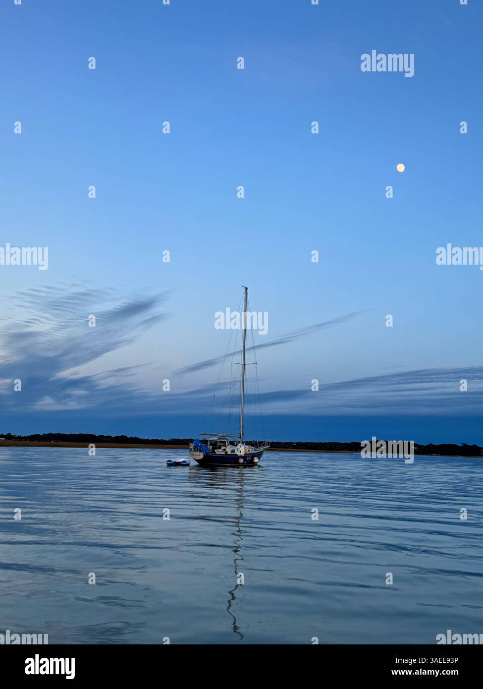 Una tranquilla barca a vela ancorata nelle calme acque costiere al crepuscolo con una luna piena che si innalza sulle Wild Dunes, Charleston, South Carolina. Foto Stock
