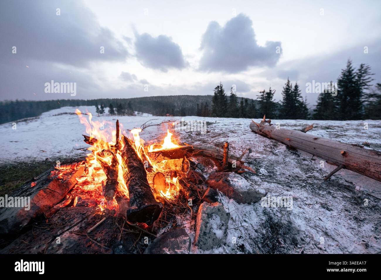 Fuoco da campeggio su un prato innevato di montagna al crepuscolo con spazio fotocopie Foto Stock