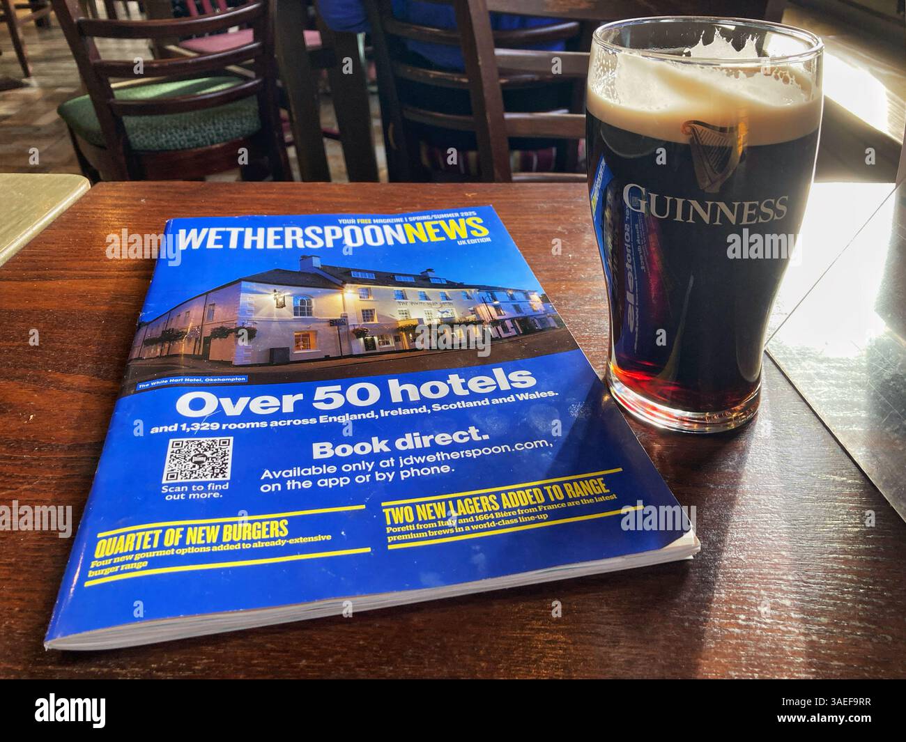 Bar e ristorante Wetherspoon che legge la rivista Wetherspoon News e serve una pinta di Guinness, Regno Unito - Immagine stock catturata con smartphone