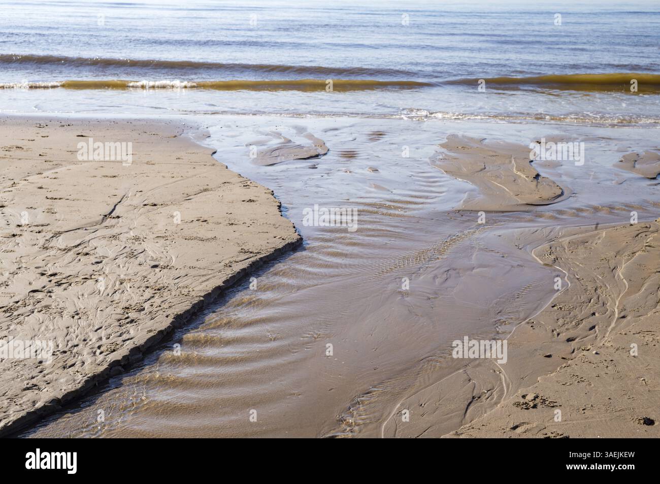 Onde delicate che scivolano sulla spiaggia di sabbia creando piccoli ruscelli d'acqua Foto Stock