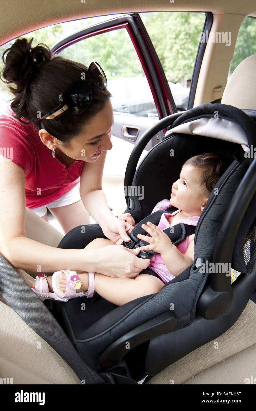 Madre felice sorridente che mette il bambino sul seggiolino e chiude la cintura per la sicurezza, New York, USA, Nord America Foto Stock