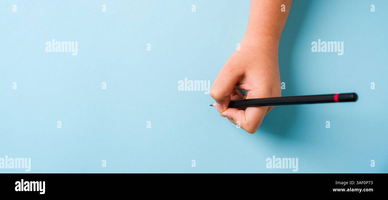 Mano sinistra con una penna a sfera su un blocco appunti aperto su sfondo blu Foto Stock