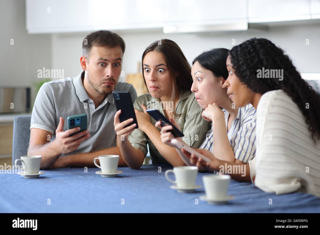 Un gruppo di amici perplessi che controllavano i telefoni in cucina a casa Foto Stock