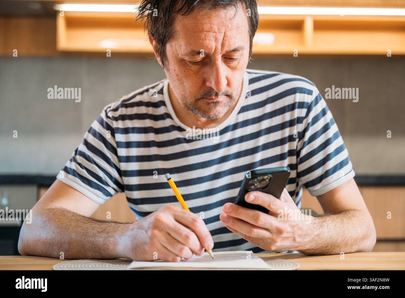 Uomo che esegue il calcolo del budget della casa utilizzando carta, matita e una calcolatrice per smartphone, messa a fuoco selettiva Foto Stock