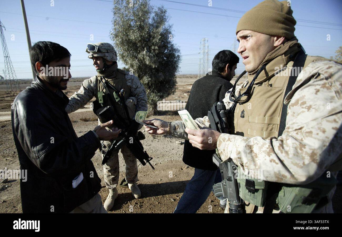 21 dicembre 2004; Fallujah, Iraq; il Maestro dei Marine PETER CASTILLO, 39 anni originario di East Chicago, Ind., distribuisce 0 banconote agli ex detenuti iracheni dopo il loro rilascio alla periferia di Fallujah, Iraq, 21 dicembre 2004. Gli uomini iracheni, tutti in età militare, sono stati arrestati durante le operazioni di combattimento a Falluja. La Combat Service Support Company 115, che trasporta provviste come cibo, acqua e munizioni ai Marines che operano a Fallujah e nei dintorni, è stata anche responsabile della gestione e del trasporto dei detenuti durante l'operazione al Fajr. Il CSSC-115 di Camp Pendleton, California, ha trasportato Foto Stock