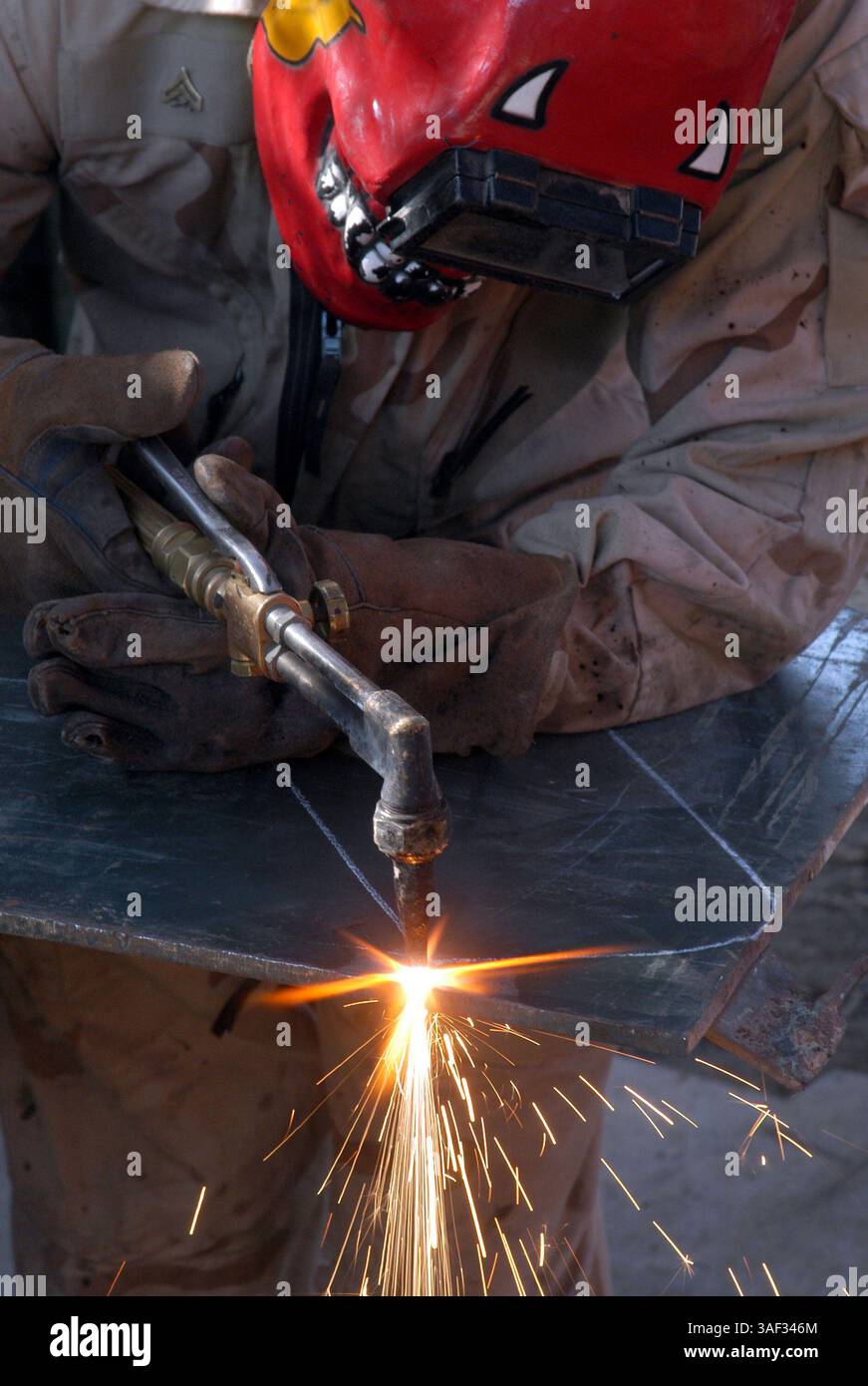 28 dicembre 2004; Camp Ramadi, Iraq; Mechanic Turned welder Cpl. BRONSON BARTLEY, 2nd Battalion, 11th Marine Regiment, 1st Marine Division taglia un pezzo di metallo che servirà come estensione per una porta Humvee, per mantenere gli occupanti all'interno più sicuri. Bronson è uno dei due caporale del 2nd Battalion, 11th Marine Regiment, 1st Marine Division accetta il lavoro di saldatura per il battaglione, anche se differisce dal loro lavoro ufficiale. Foto Stock