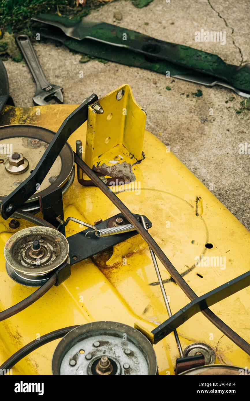 Osservare attentamente i componenti meccanici di un rasaerba giallo su cemento Foto Stock