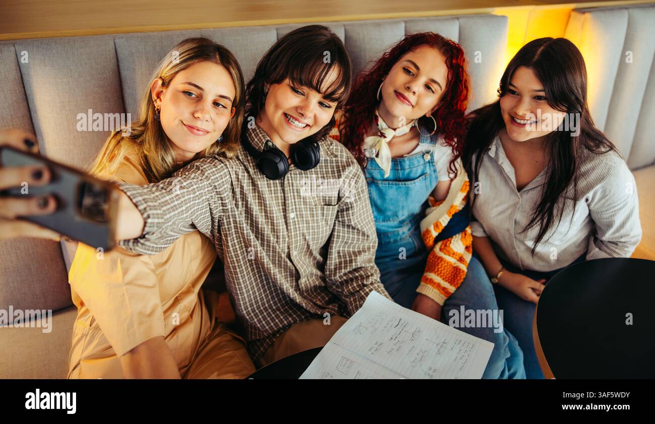 Un gruppo di allegri compagni di classe che scattano un selfie durante una riunione di progetto di gruppo, illustrando collaborazione e amicizia in un ambiente confortevole. Foto Stock