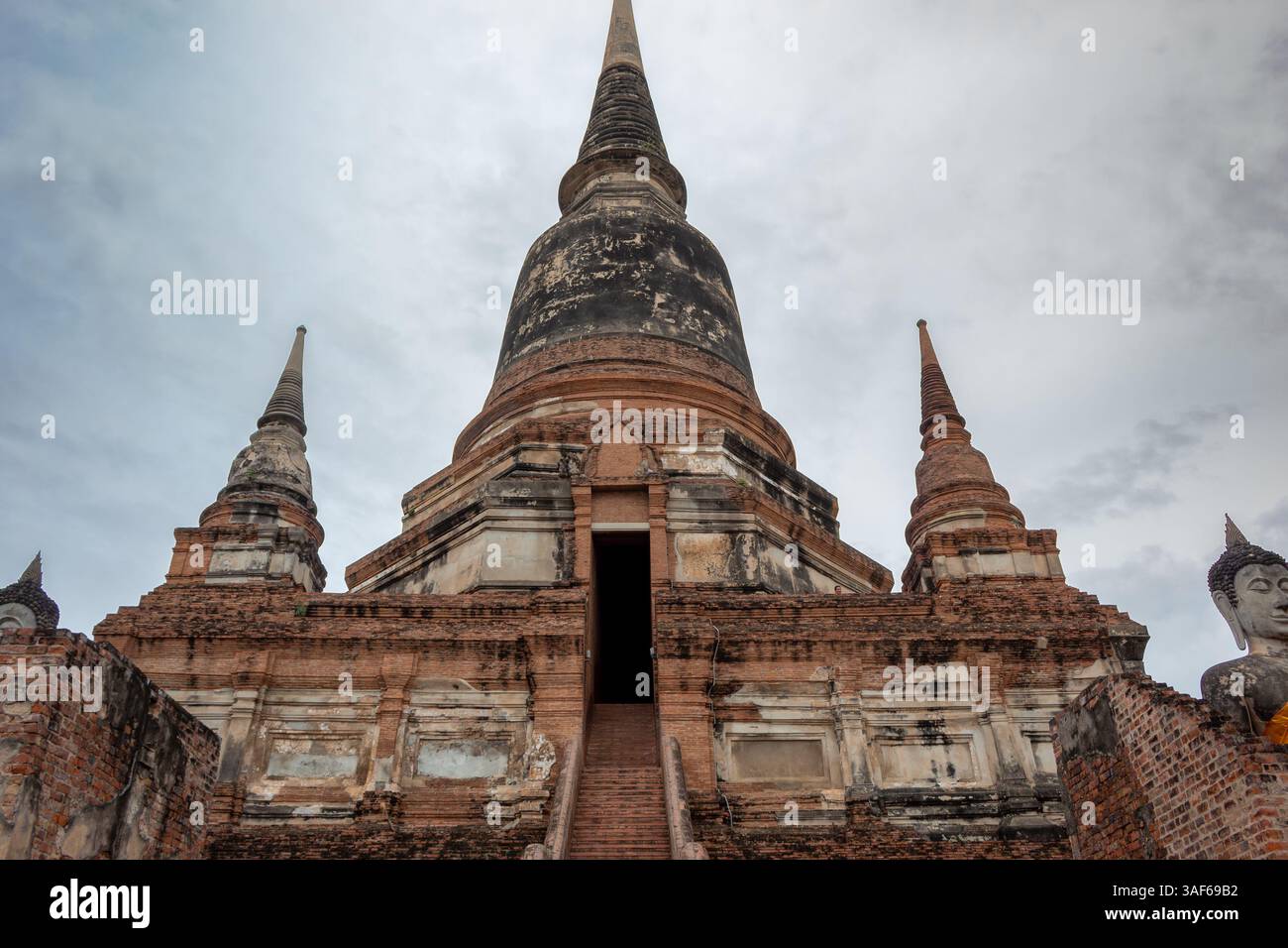 Edificio in mattoni rossi e templi in pietra in rovina e statua di buddha in oro del parco storico Wat Yai Chai Mongkhon ad Ayutthaya in Thailandia Foto Stock