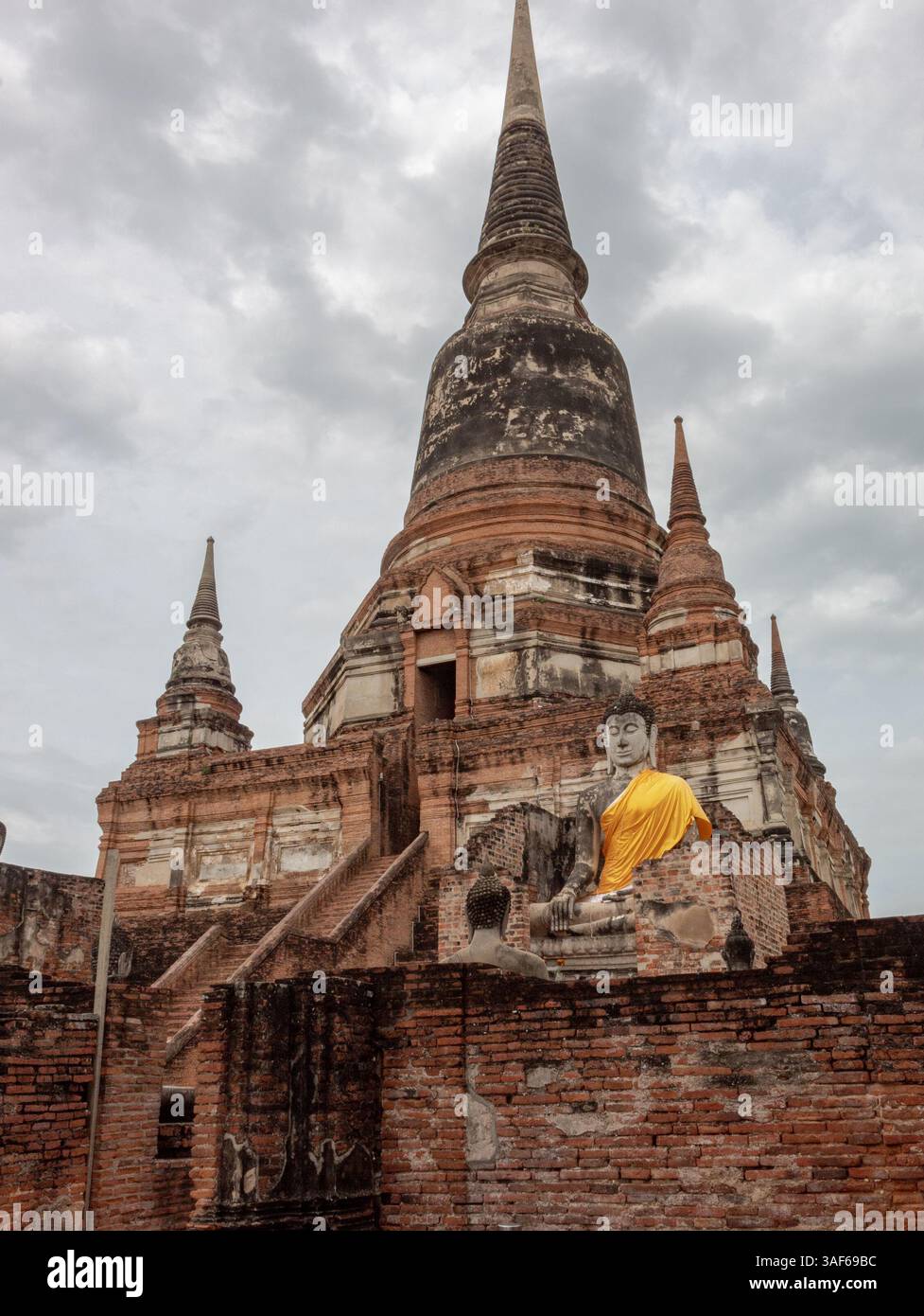 Edificio in mattoni rossi e templi in pietra in rovina e statua di buddha in oro del parco storico Wat Yai Chai Mongkhon ad Ayutthaya in Thailandia Foto Stock