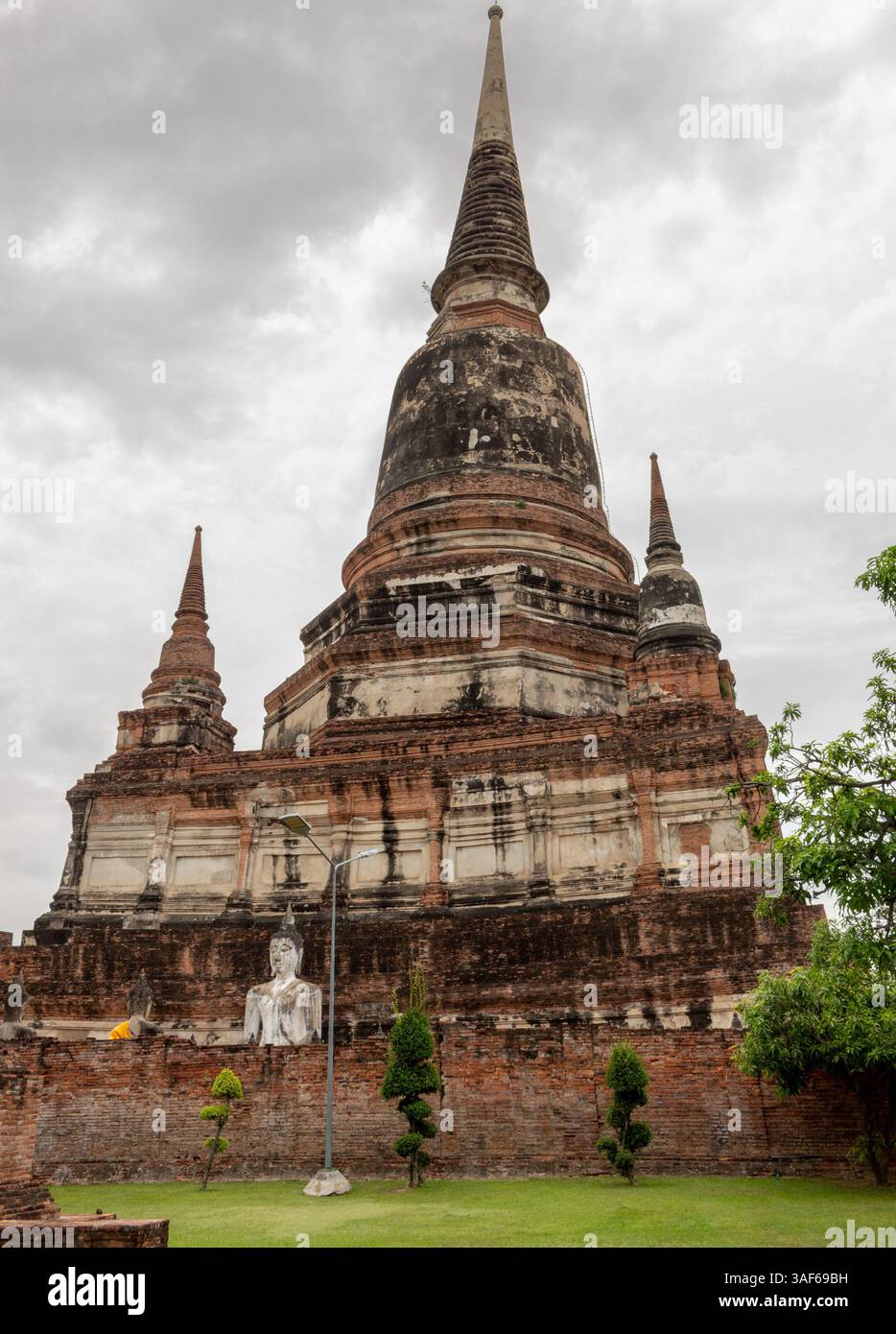 Edificio in mattoni rossi e templi in pietra in rovina e statua di buddha in oro del parco storico Wat Yai Chai Mongkhon ad Ayutthaya in Thailandia Foto Stock