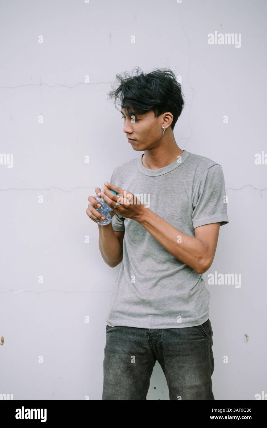 Un giovane asiatico in un abbigliamento casual, con una bottiglia d'acqua di plastica sullo sfondo. Scatto concettuale per rinfreschi e uno stile di vita attento Foto Stock