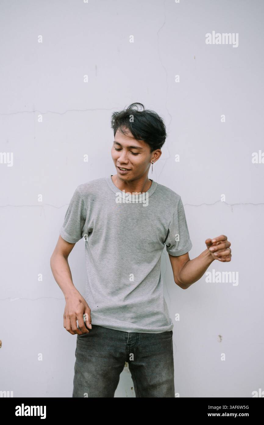 Giovane uomo asiatico con un abbigliamento casual in piedi su un semplice sfondo bianco mentre indossa una t-shirt grigia Foto Stock