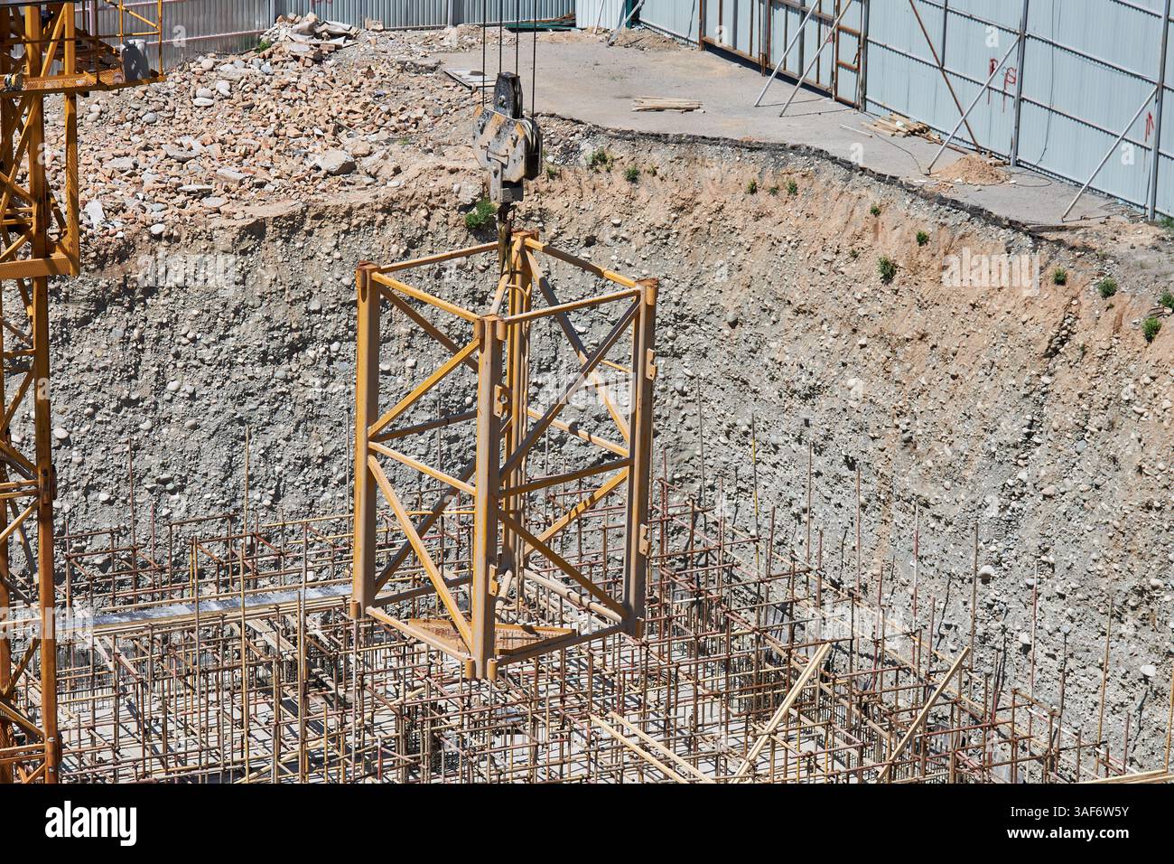 Una gru da cantiere solleva un'ulteriore sezione di gru su un gancio per aumentare l'altezza. Cantiere, pozzo di fondazione Foto Stock