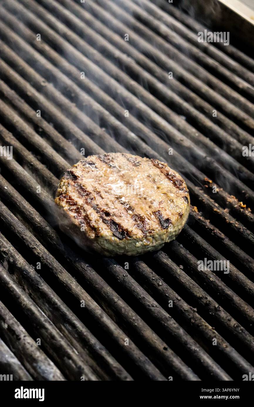 Classico hamburger patti su un barbecue grigliato con fumo in uscita Foto Stock