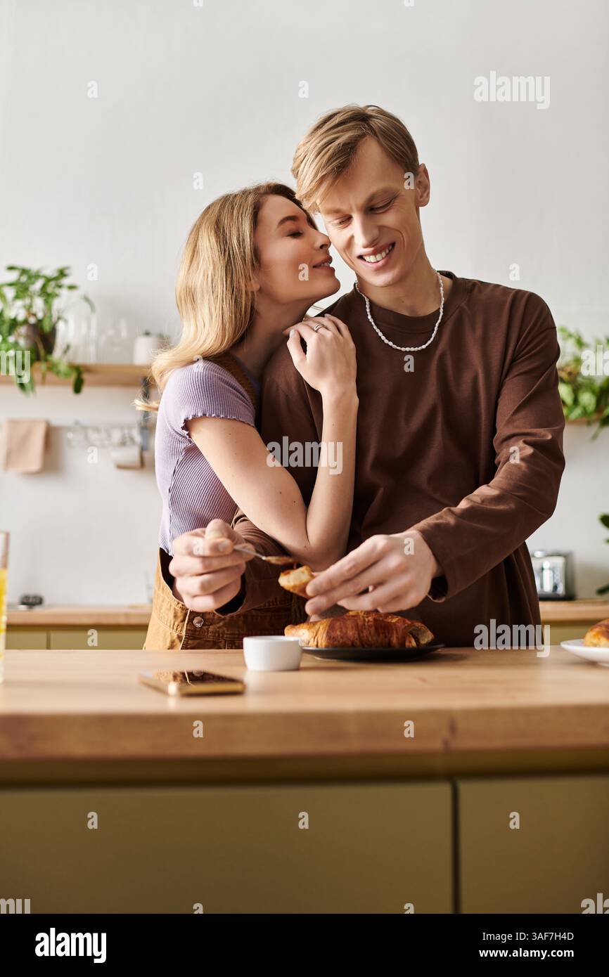 In una cucina accogliente, una giovane coppia gode di un momento intimo insieme, sorridendo e condividendo il cibo. Foto Stock