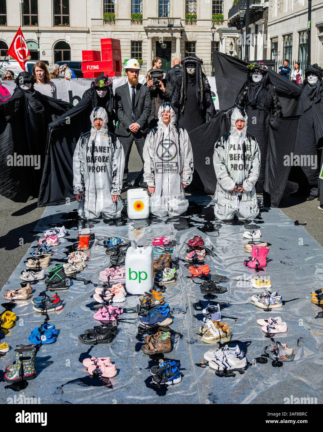 Londra, Regno Unito. 7 aprile 2025. Un manifestante vestito da dirigente della BP, e supportato da petroliere in vesti nere, versava olio su ribelli inginocchiati, e poi su file di scarpe vuote per bambini davanti all'edificio, simboleggiando ciò che la strategia della BP a U significa per il futuro dei nostri figli. Gli attivisti di età compresa tra i 4 e i 83 anni hanno occupato la strada fuori dal quartier generale di Londra di St James's Square della BP per chiedere al gigante petrolifero di invertire la loro decisione di rottamare la precedente strategia di transizione energetica sostenuta dagli azionisti. Il volto del CEO, Auchincloss, è apparso sui cartelli che recitano: "RICERCATO per distruggere i nostri Futures". Credito Bell/Alamy Foto Stock