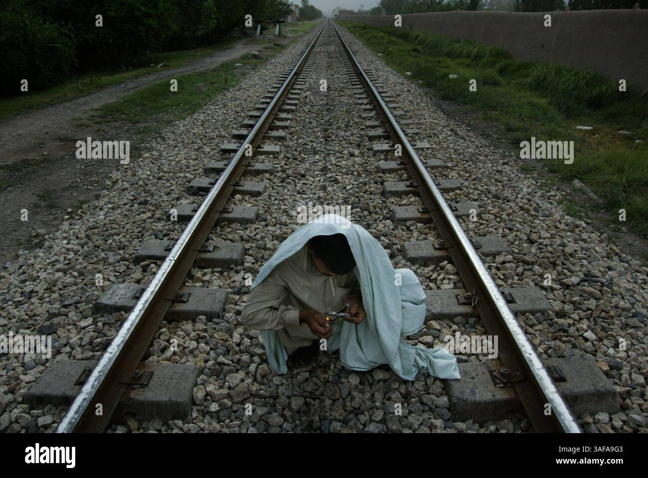 07 giu 2006 - Peshawar, NWFP, Pakistan - il percorso di un binario ferroviario porta a un tossicodipendente che accende l'eroina. Migliaia di eroine tossicodipendenti vivono nelle acque reflue sotto i ponti del Pakistan occidentale. La maggior parte di loro rubano per pagare le droghe, che sono economiche e facilmente accessibili. A causa della loro dipendenza dalla droga e delle condizioni di vita deplorevoli, molti consumatori muoiono giovani. Il numero di centri di riabilitazione riusciti è prossimo allo zero. La data è approssimativa (immagine di credito: Jenna Schoenefeld/ZUMAPRESS.com) Foto Stock