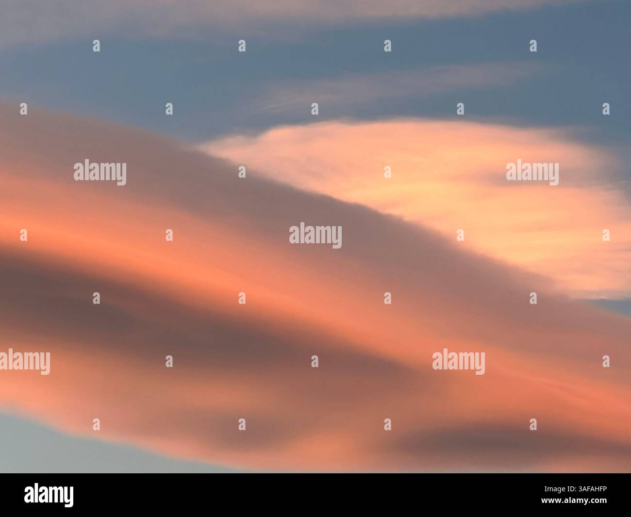 Vista accattivante delle nuvole a strati dipinte in vivaci tonalità rosa e arancione su un cielo blu. Foto Stock
