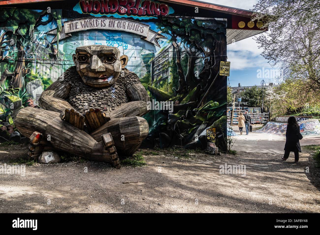 Copenaghen, Danimarca. 6 aprile 2025. Una gigantesca scultura di troll in legno (Green George) realizzata da Thomas Dambo posta di fronte a un muro con graffiti o murales visti al Freetown Christiania. Domenica pomeriggio, un tavolo è stato preparato per un caffè e una torta a Pusher Street a Freetown Christiania. (Foto di Kristian Tuxen Ladegaard Berg/SOPA Images/Sipa USA) credito: SIPA USA/Alamy Live News Foto Stock