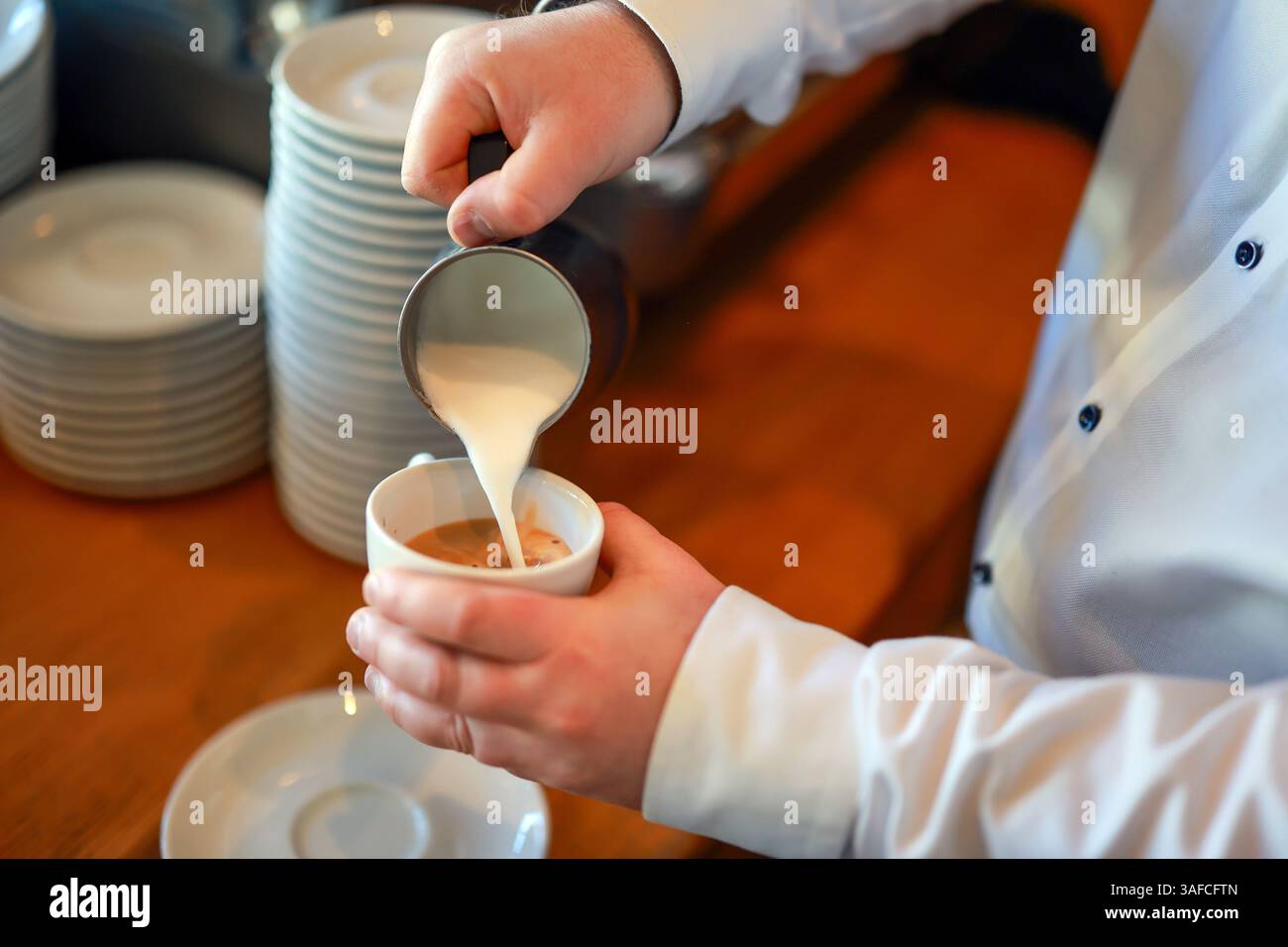 Germania - il barista prepara un caffè, qui un cappuccino, versa a mano la schiuma di latte da una piccola caffettiera in una tazza di caffè espresso. Foto Stock