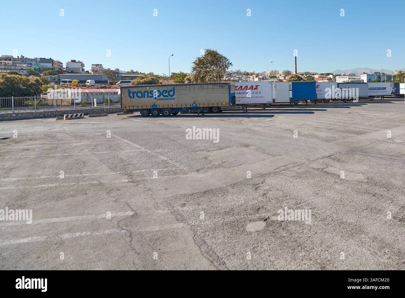 Creta, Grecia - 7 aprile 2025: Area di parcheggio per camion circondata da recinzioni e alberi, evidenziando la sua disposizione organizzata per i veicoli logistici con ampio spazio Foto Stock
