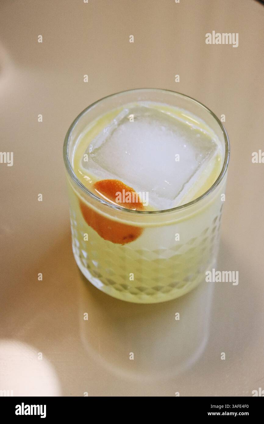 Elegante cocktail di agrumi con cubetto di ghiaccio e scorza d'arancia in vetro testurizzato su sfondo neutro - vista dall'alto Foto Stock
