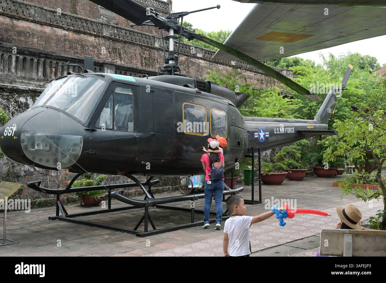 VIETNAM, Hanoi, Museo militare, equipaggiamento militare e rottami di guerra della guerra coloniale francese del 1946-1954 e della guerra americana in Vietnam del 1955 - 1975, visitatore vietnamita all'elicottero americano Iroquois UH-1H / VIETNAM, Hanoi, Museo Militär, Ausstellung mit Waffen zum Krieg der Amerikaner in Vietnam, Vietnamesische Besucher an einem US Helikopter Foto Stock