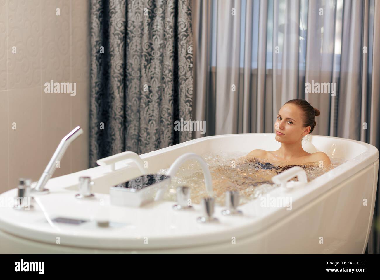 Bella giovane donna che si rilassa in una vasca idromassaggio presso il lussuoso centro benessere per il benessere e il ringiovanimento. Foto Stock