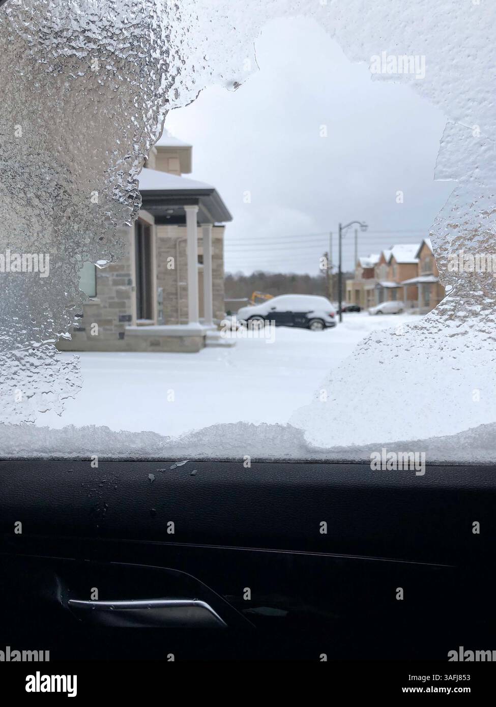 Uno strato di ghiaccio sul finestrino dell'auto dopo una tempesta di ghiaccio invernale che si affaccia sul quartiere residenziale innevato Foto Stock
