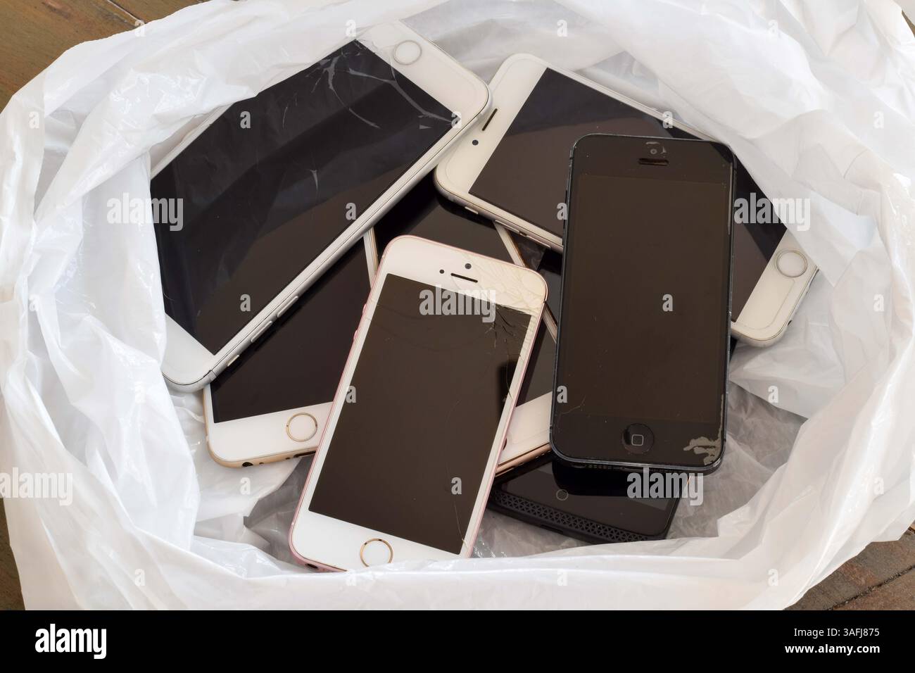 4 aprile 2025 - Newmarket, Ontario, Canada: Una collezione di vecchi iPhone obsoleti rotti in un sacco di rifiuti bianchi, che illustrano i rifiuti tecnologici Foto Stock