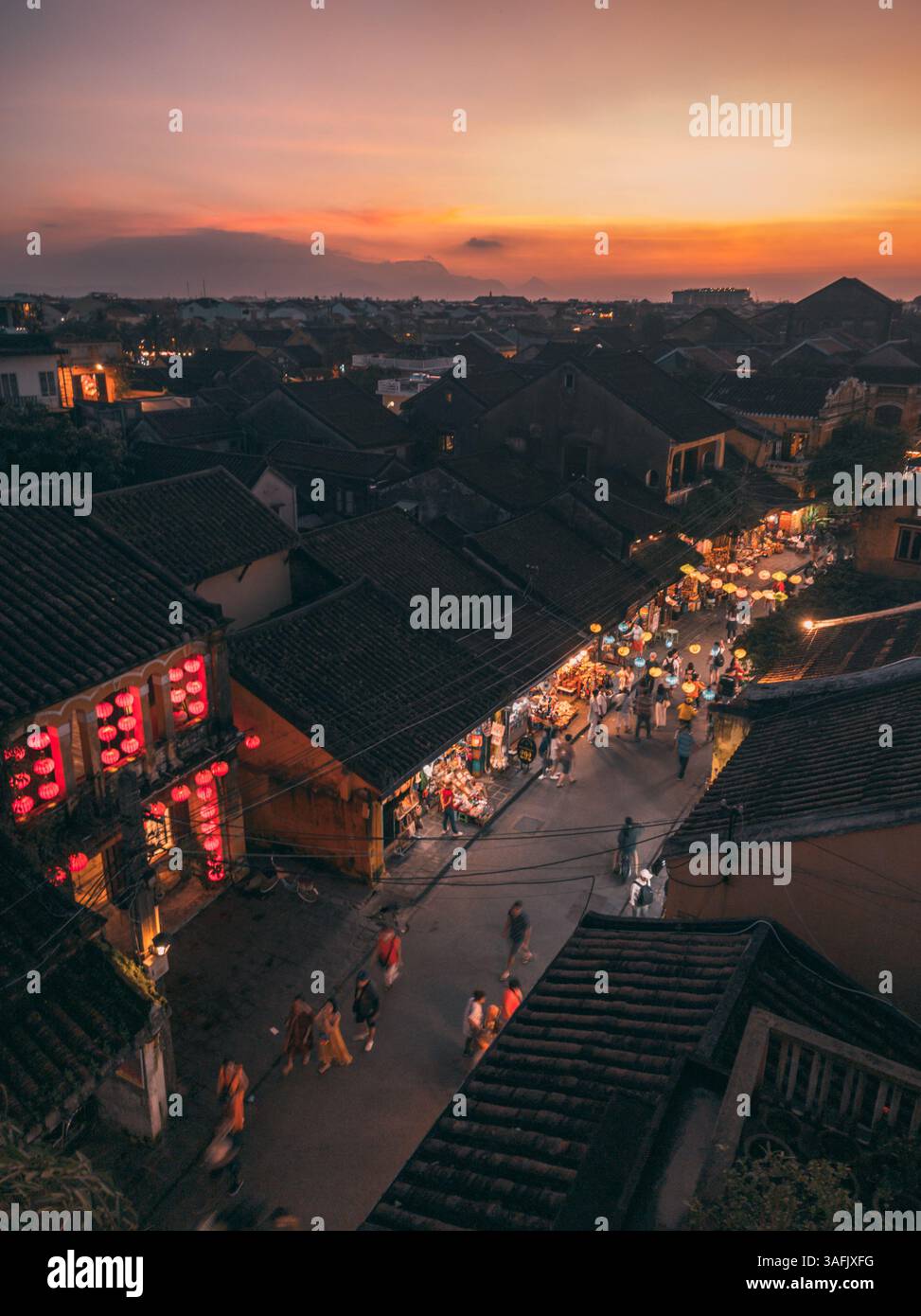 Il crepuscolo dorato bagna le strade storiche di Hoi An, Vietnam, mentre i sentieri illuminati da lanterne e la vivace energia creano un'atmosfera incantevole e indimenticabile Foto Stock